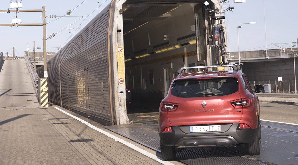 A red car driving onto a Eurotunnel Le Shuttle train from the platform